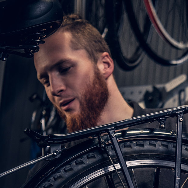 Two bearded mechanics fixing town bicycle in a workshop.